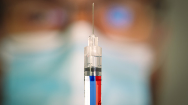 Close-up of hypodermic syringe with the Russian Federation flag and a blurred doctor on the background. Selective focus. Concept of Covid vaccination campaign in Russia