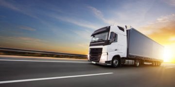 European truck on motorway with beautiful sunset sky and dramatic clouds. Transportation and cargo theme, free space for text.