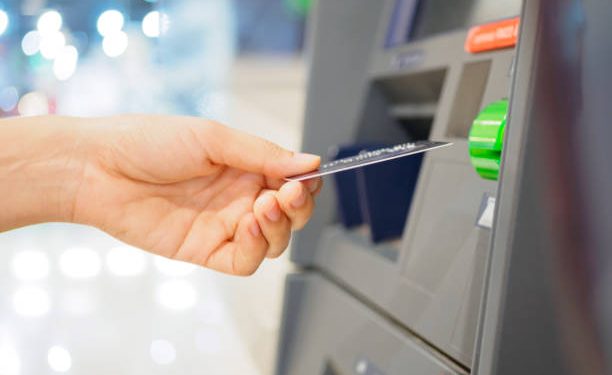 Close-up of woman's hand inserting debit card into an ATM machine. Horizontal shot.
