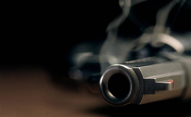 A gritty crime scene image of a smoking hand gun, revolver, lying on the floor with narrow focus on the tip if the barrel and dark background