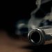 A gritty crime scene image of a smoking hand gun, revolver, lying on the floor with narrow focus on the tip if the barrel and dark background
