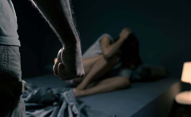Man threatening a woman in the bedroom, she is scared and lying in bed, domestic violence concept