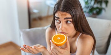 Sick woman trying to sense smell of half fresh orange, has symptoms of Covid-19, corona virus infection - loss of smell and taste. One of the main signs of the disease.