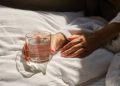 A glass of water next to a girl sleeping in bed. Happy morning. Woman in pyjamas. Healthy lifestyle, wellness. Proper nutrition. Drinking water. Morning with water. Sunlight on linens. Pillow, blanket