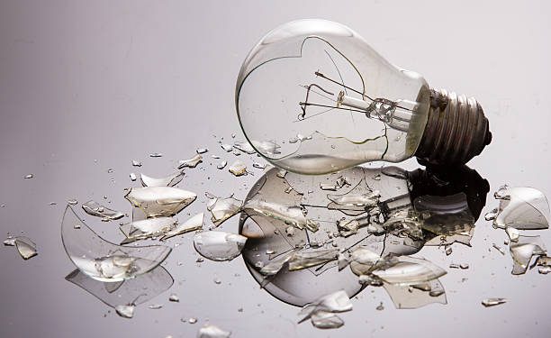 Broken light bulb on shiny surface with pieces backlit