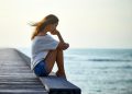 Sad lonely beautiful woman sitting on the pier with copy space